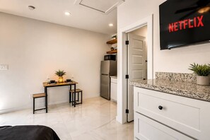 A modern kitchen with a built-in refrigerator, a dining area with a table and chairs, and a wall-mounted television displaying 'NETFLIX'. - #11 | Boutique SPI Studio | Pool Walk2 Beach WiFi (South Padre Island)