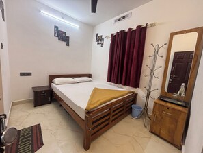 A bedroom with a bed, a wooden dresser, a mirror, a coat rack, and a welcome mat. - Serene 4-bedroom house in charming Suryanelli perfect for relaxing getaway (Suryanelli)