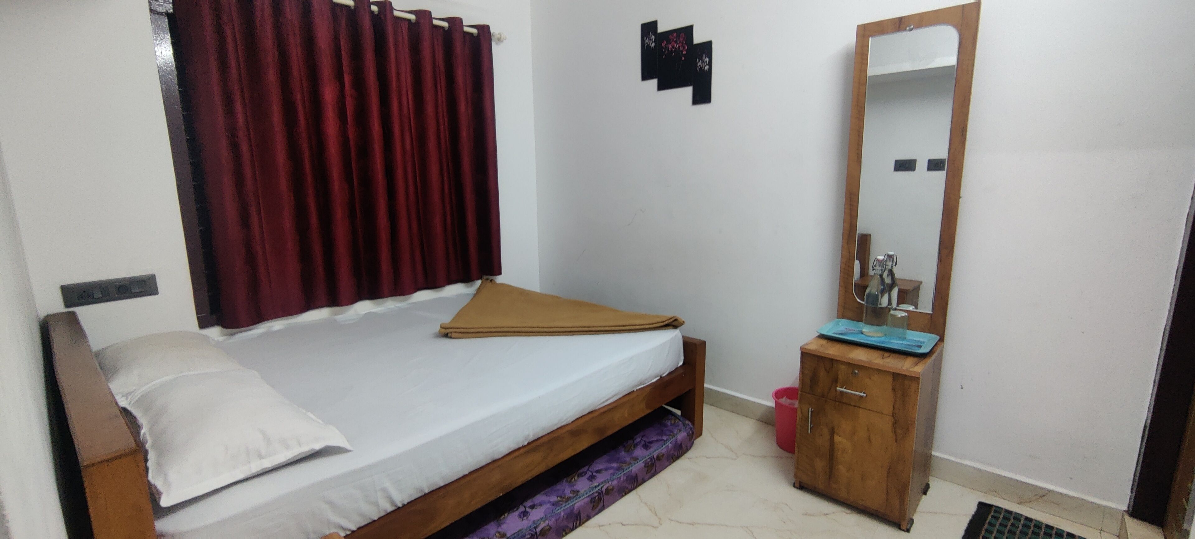 A bedroom with a single bed, a wooden nightstand, a mirror, and a red curtain.