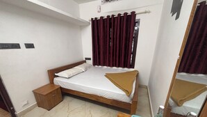 A bedroom with a bed, a nightstand, a mirror, and a window with curtains.
