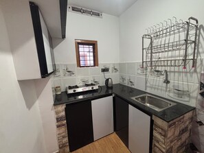 A compact kitchen with a gas stove, a sink, and a drying rack. - Serene 4-bedroom house in charming Suryanelli perfect for relaxing getaway (Suryanelli)