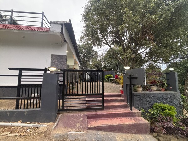 A gated entrance with steps leading to a building, surrounded by greenery and a stone wall.