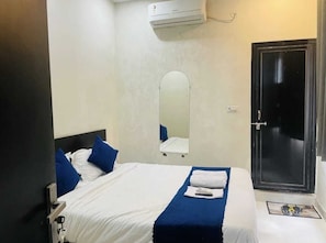 A hotel room with a bed, a mirror, a door, and an air conditioning unit. - Get Book Hotel (Udaipur)