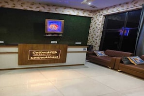 A reception area with a GetbookCab sign, a television, and a brown leather sofa. - Get Book Hotel (Udaipur)