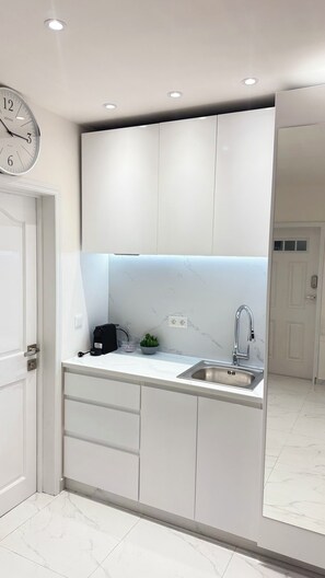 A modern kitchen with white cabinets, a stainless steel sink, and a clock on the wall. - The Little Heaven Retreats - Studio (Saint-martin)
