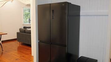 Een moderne keuken met een zwarte koelkast, houten vloeren en een kleine prullenbak.