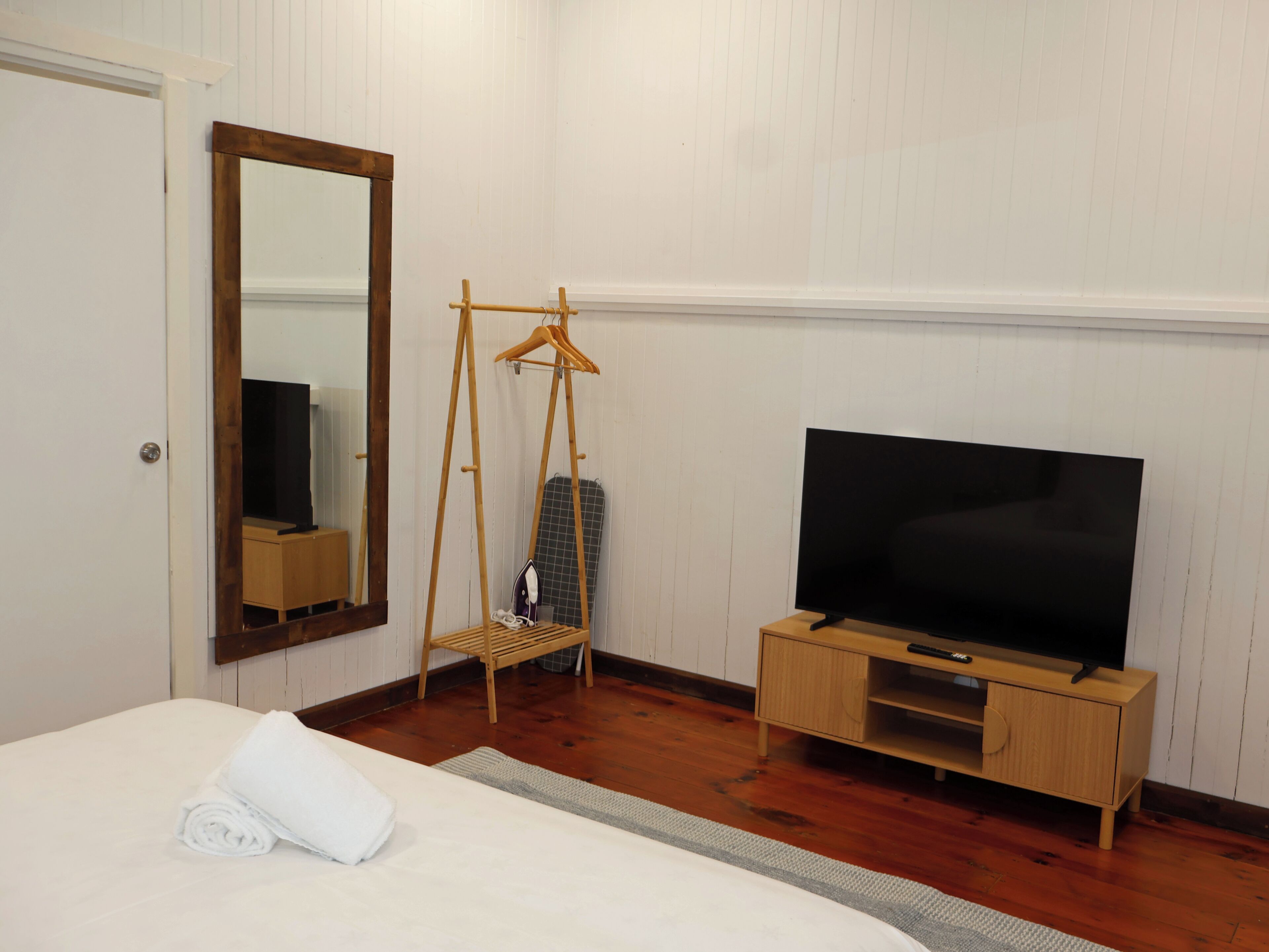Habitación de hotel con cama, televisor sobre un soporte de madera, espejo y un tendedero de madera.