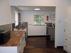 A kitchen with a wooden countertop, white cabinets, a stainless steel sink, and a window with blinds. - Gympie Cottage (Gympie)