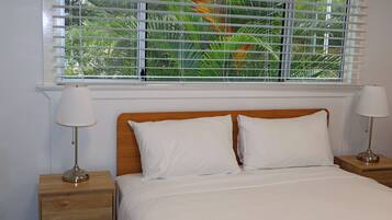 Een bed met wit beddengoed, twee bedlampjes en een raam met zonwering.