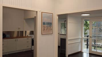 A room with a wooden floor, white walls, a kitchen area with cabinets and a stove, and a door leading to an outdoor area.