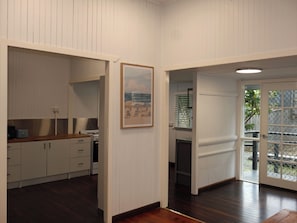 A room with a wooden floor, white walls, a kitchen area with cabinets and a stove, and a door leading to an outdoor area.