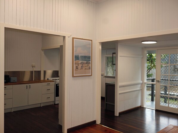 A room with a wooden floor, white walls, a kitchen area with cabinets and a stove, and a door leading to an outdoor area.
