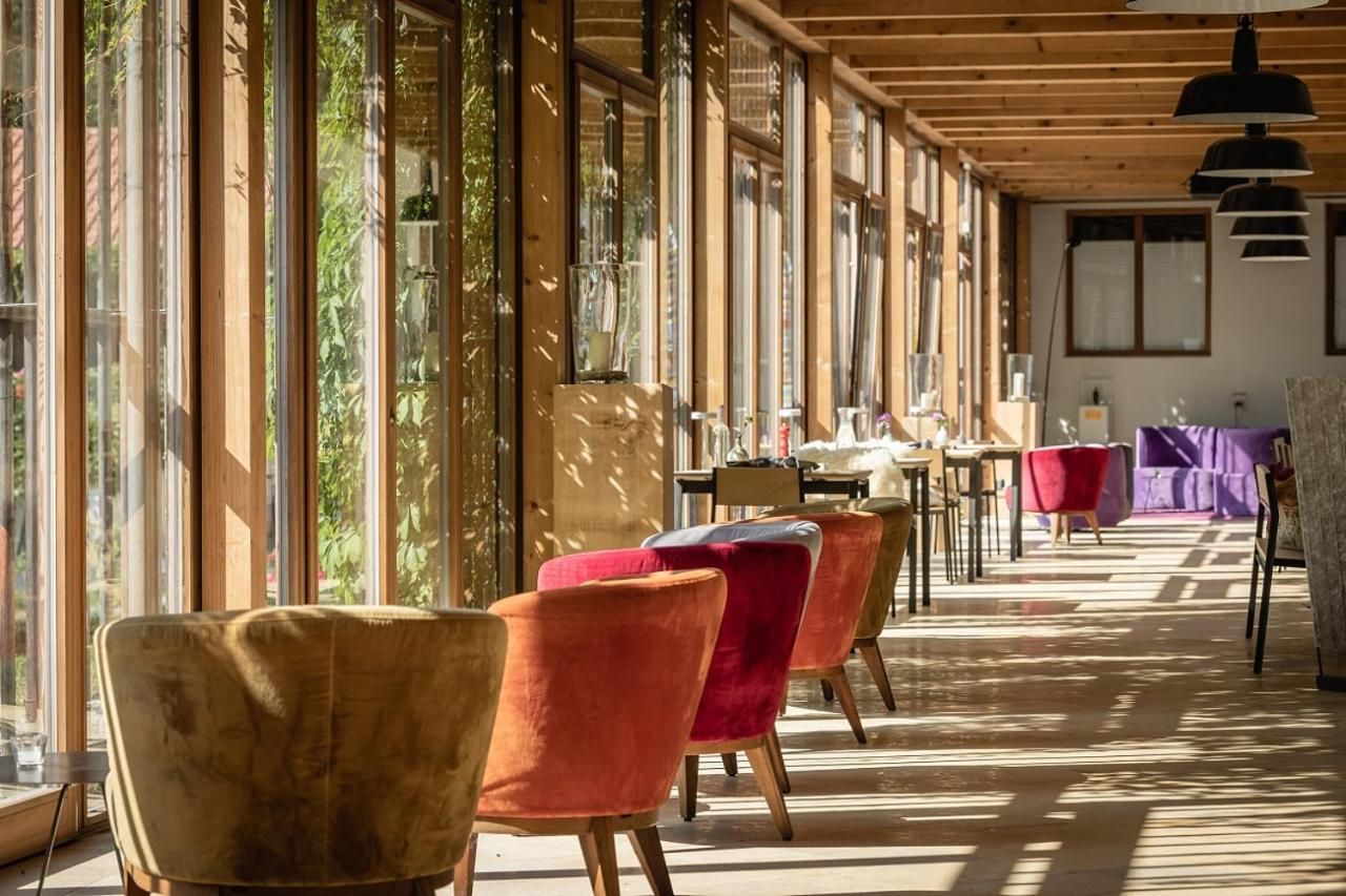 Ein Zimmer mit großen Fenstern, Holzbalken und einem langen Tisch mit Stühlen.