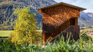 Eine Holzhütte mit geneigtem Dach, eingebettet in eine gebirgige Landschaft und einem Baum.