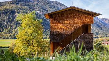 Eine Holzhütte mit geneigtem Dach, eingebettet in eine gebirgige Landschaft und einem Baum.