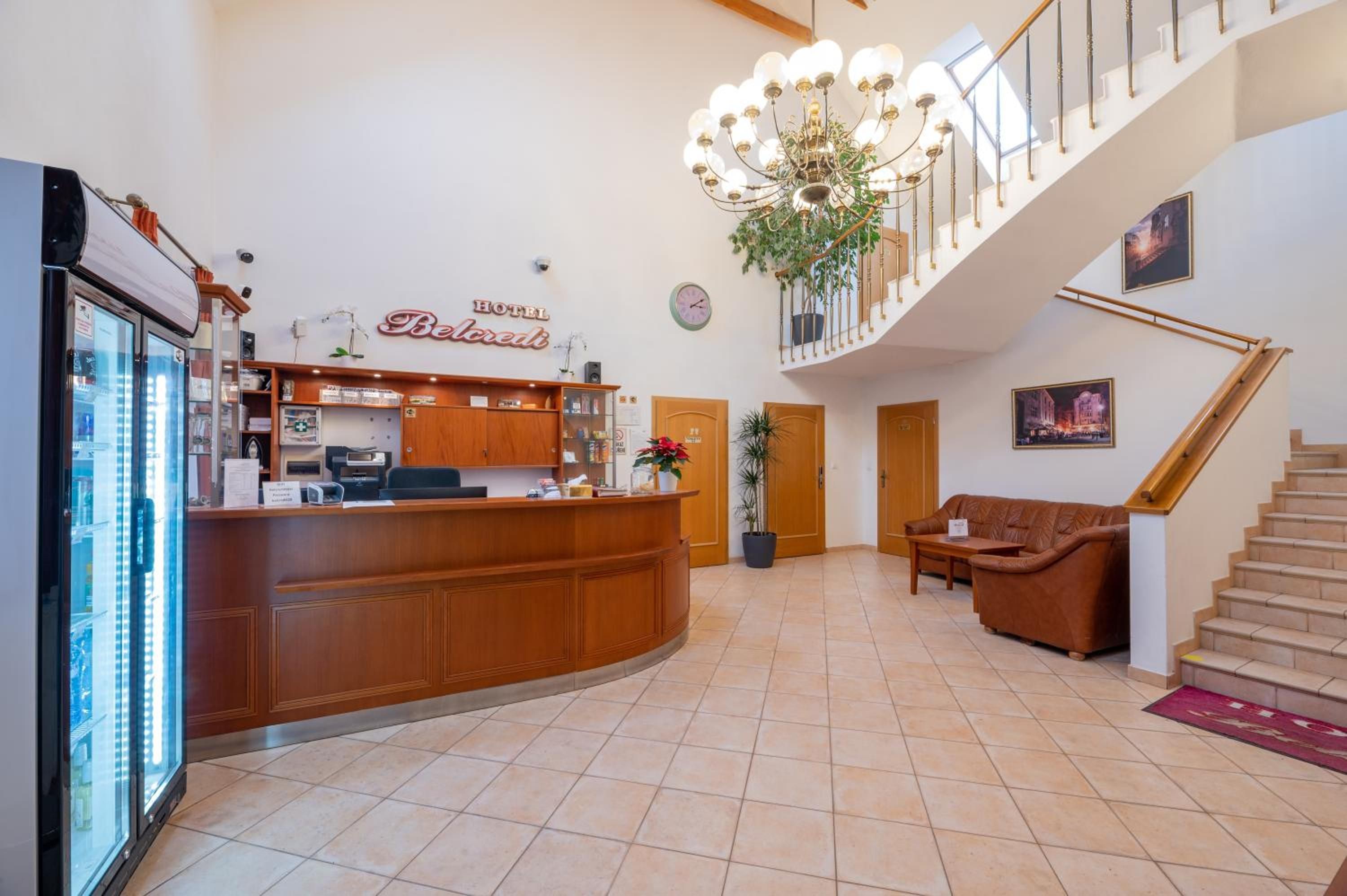 Zona de recepción de un hotel con mostrador de madera, candelabro, escalera y sofá.