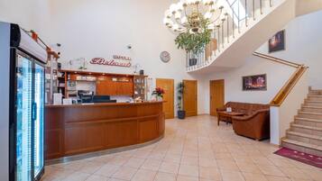 Zona de recepción de un hotel con mostrador de madera, candelabro, escalera y sofá.
