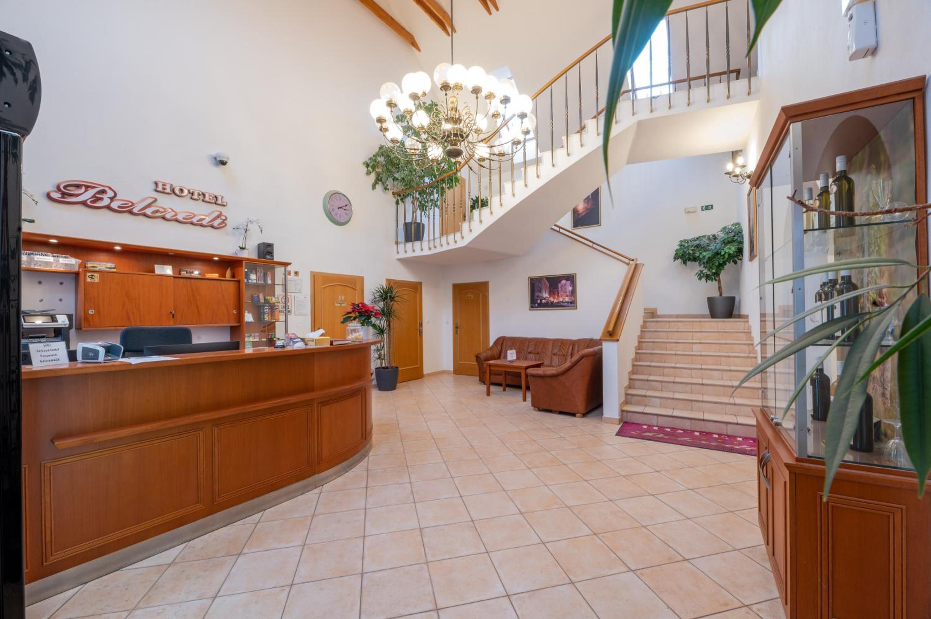 A hotel lobby with a reception desk, a staircase, and a chandelier.