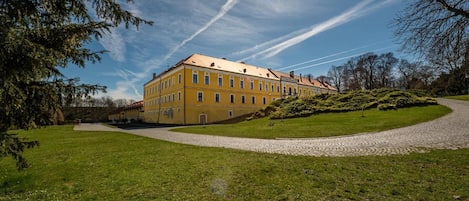 A large yellow building with multiple windows, surrounded by a well-maintained lawn and a gravel path leading to the entrance.
