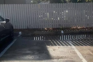 Un estacionamiento con cerca blanca y un coche aparcado a la izquierda.