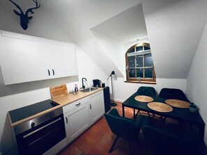 A compact kitchen with white cabinets, a black countertop, and a dining area with a table and chairs. - Oldenburger Mvºhle (Oldenburg)