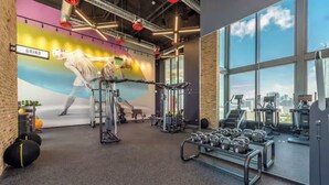 Uma academia com equipamentos de ginástica, um mural e grandes janelas.