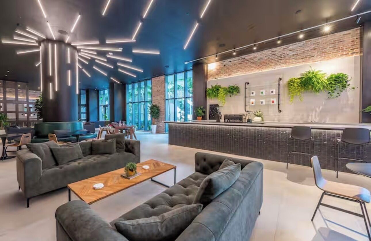 A modern lounge area with sofas, a wooden coffee table, and a bar with a brick wall backdrop.
