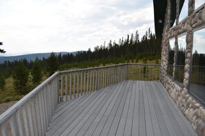 Eine Holzterrasse mit einer Steinmauer und einem Metallgeländer, mit Blick auf eine bewaldete Landschaft.