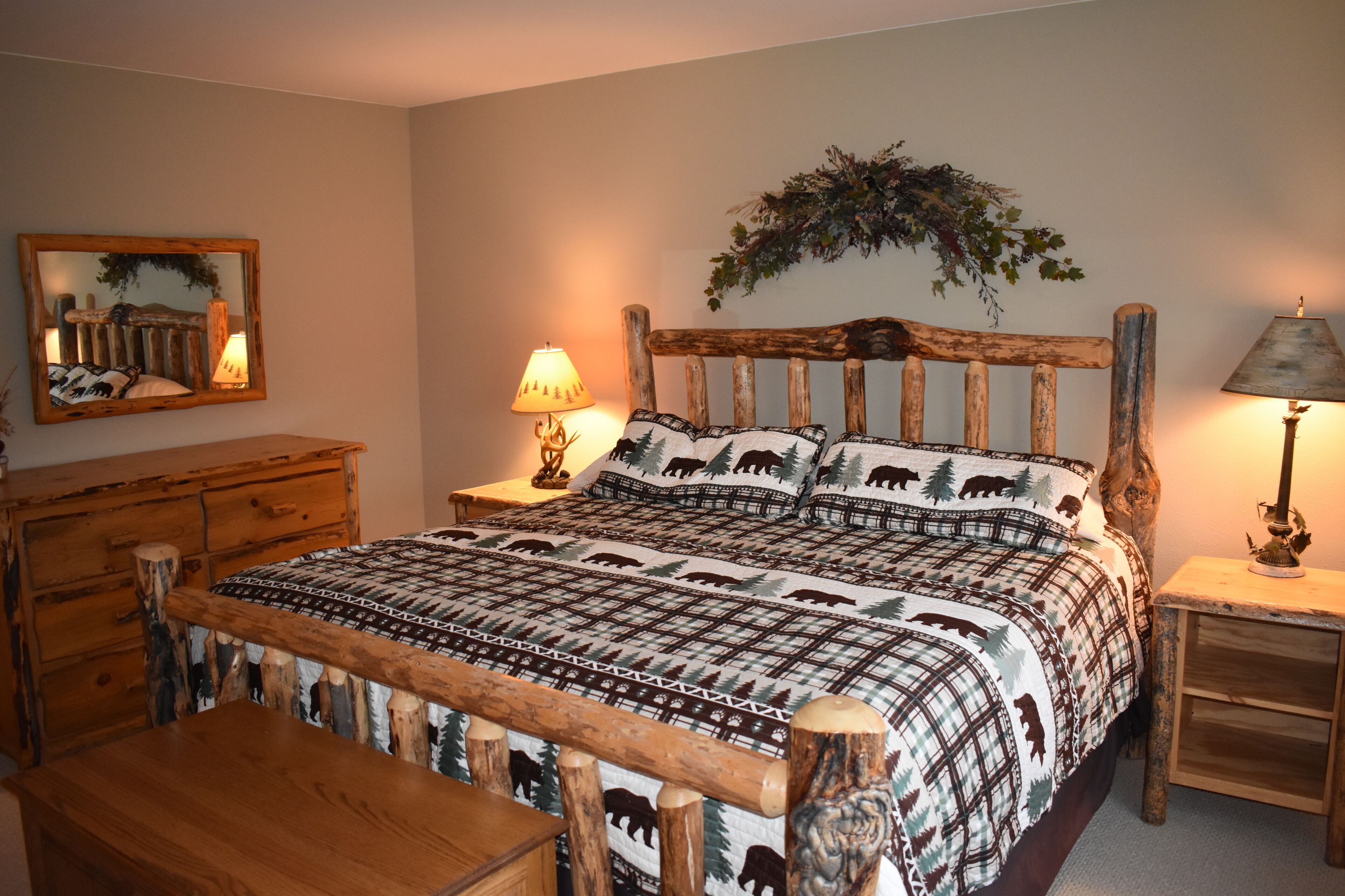 A bedroom with a wooden bed frame, a bedside table with a lamp, a dresser, and a mirror on the wall.