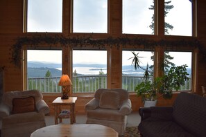 Una habitación acogedora con dos sillones, una mesita y vistas a un lago y montañas a través de amplios ventanales.