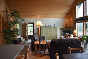 A cozy cabin interior with a fireplace, wooden furniture, and a staircase leading to an outdoor area. - Mountainside Georgetown Lake Cabin with Sweeping Lake & Pintler Mountain Views (Anaconda)