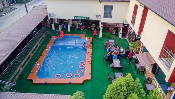 Una piscina amb un solàrium al voltant, una zona de seients amb taules i cadires, i un edifici amb un rètol que diu 'Heineken'.