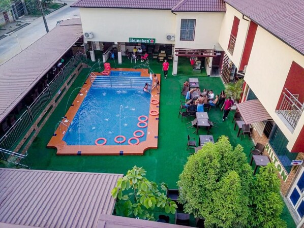 A swimming pool with a surrounding deck, a seating area with tables and chairs, and a building with a sign that reads 'Heineken'. - Villa Hilton Hotels and Apartments (Uyo)