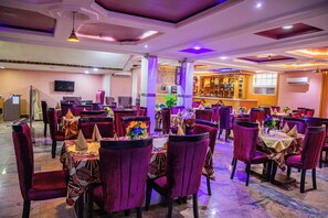 A restaurant with multiple tables and chairs, a bar area, and a television screen on the wall. - Villa Hilton Hotels and Apartments (Uyo)