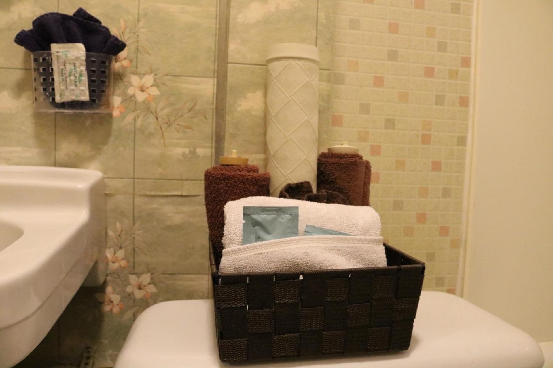 A bathroom with a toilet, a basket containing toiletries, and a towel rack with towels.