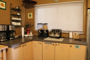 A kitchenette with a coffee maker, toaster, and storage cabinets labeled for employees.