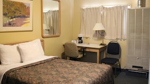 Ein Hotelzimmer mit Bett, Schreibtisch, Stuhl, Lampe, einem fenster mit Vorhängen, einer Heizung und einem Bild an der Wand.