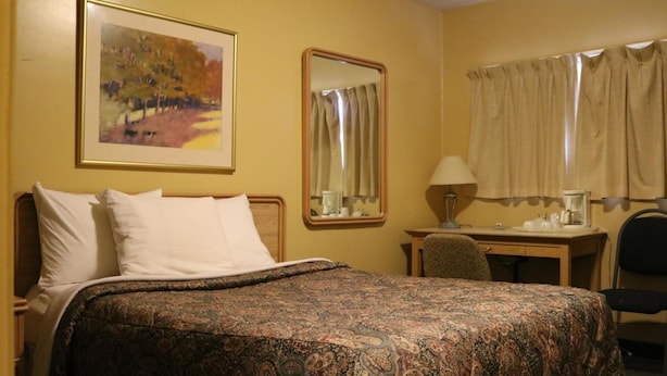 Ein Hotelzimmer mit Bett, Schreibtisch, Stuhl, Spiegel und einem Fenster mit Vorhängen.