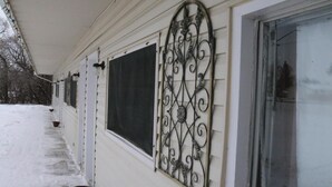 Ein Haus mit überdachter Veranda, einem großen Fenster mit dekorativem Metallgitter und verschneitem Grund.