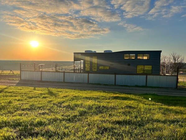 A modern building with a flat roof, large windows, and a fenced outdoor area. - Hillside Acres Tiny Home (Minkler)