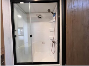 A glass-enclosed shower stall with a showerhead and hose. - Hillside Acres Tiny Home (Minkler)