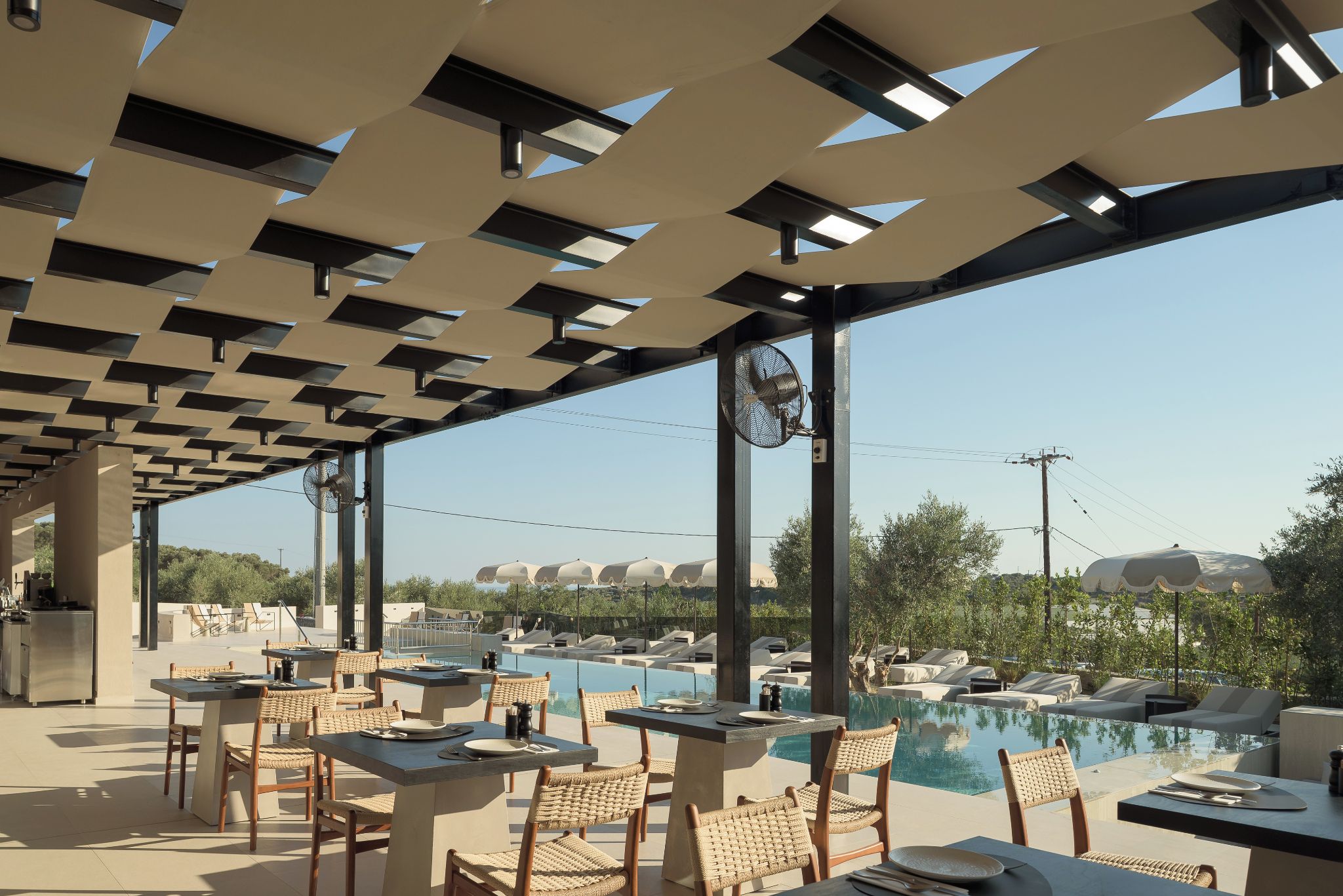 Un área de piscina al aire libre con sillones y mesas, rodeada por una estructura de pérgola.