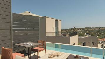 A rooftop pool area with a table and chairs, a lounge chair, and a view of the surrounding landscape.