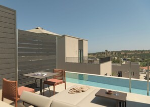 Un área de piscina en la azotea con una mesa y sillas, un sillón de descanso y vistas del paisaje circundante.