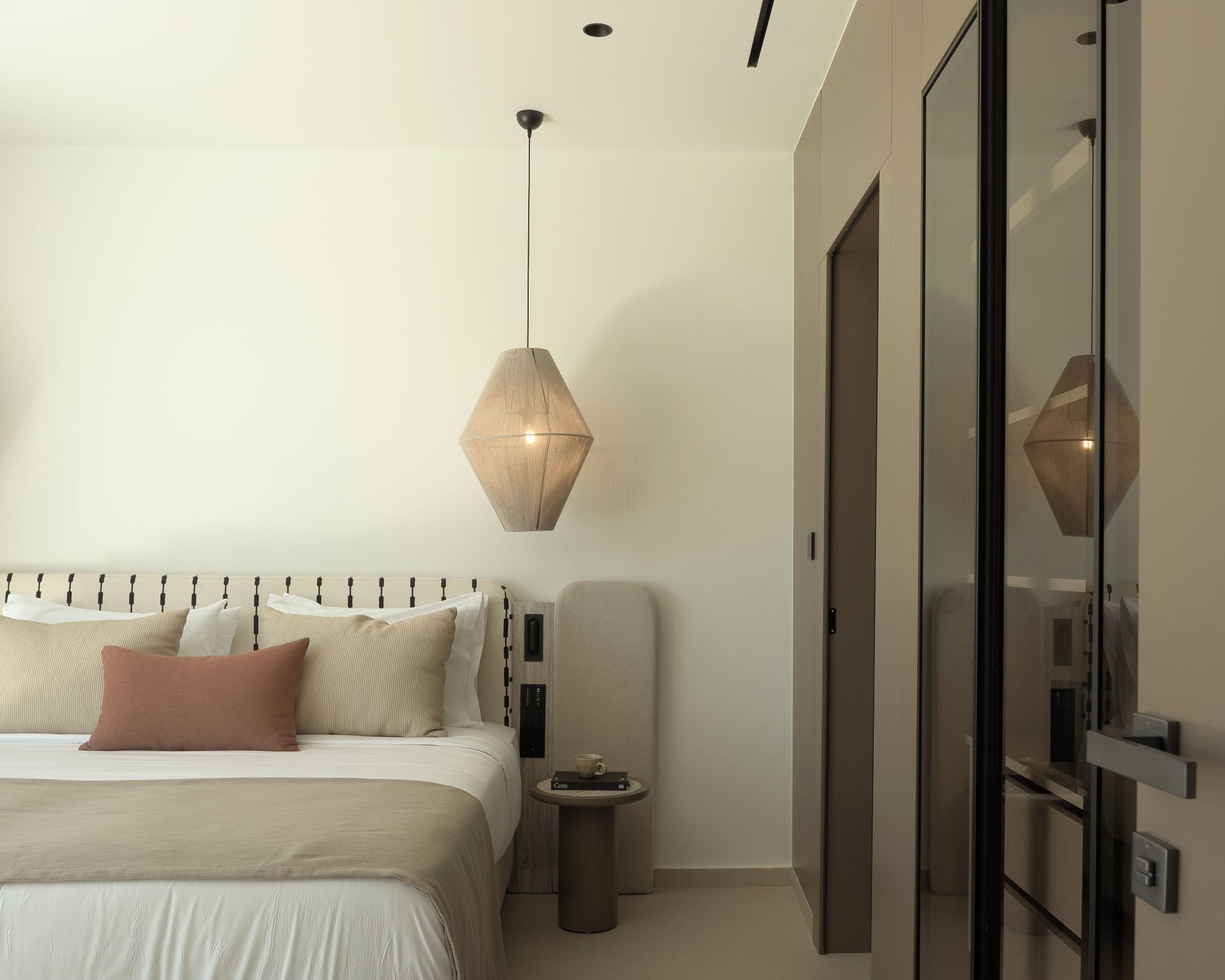 A modern bedroom with a bed, bedside table, and a hanging light fixture.