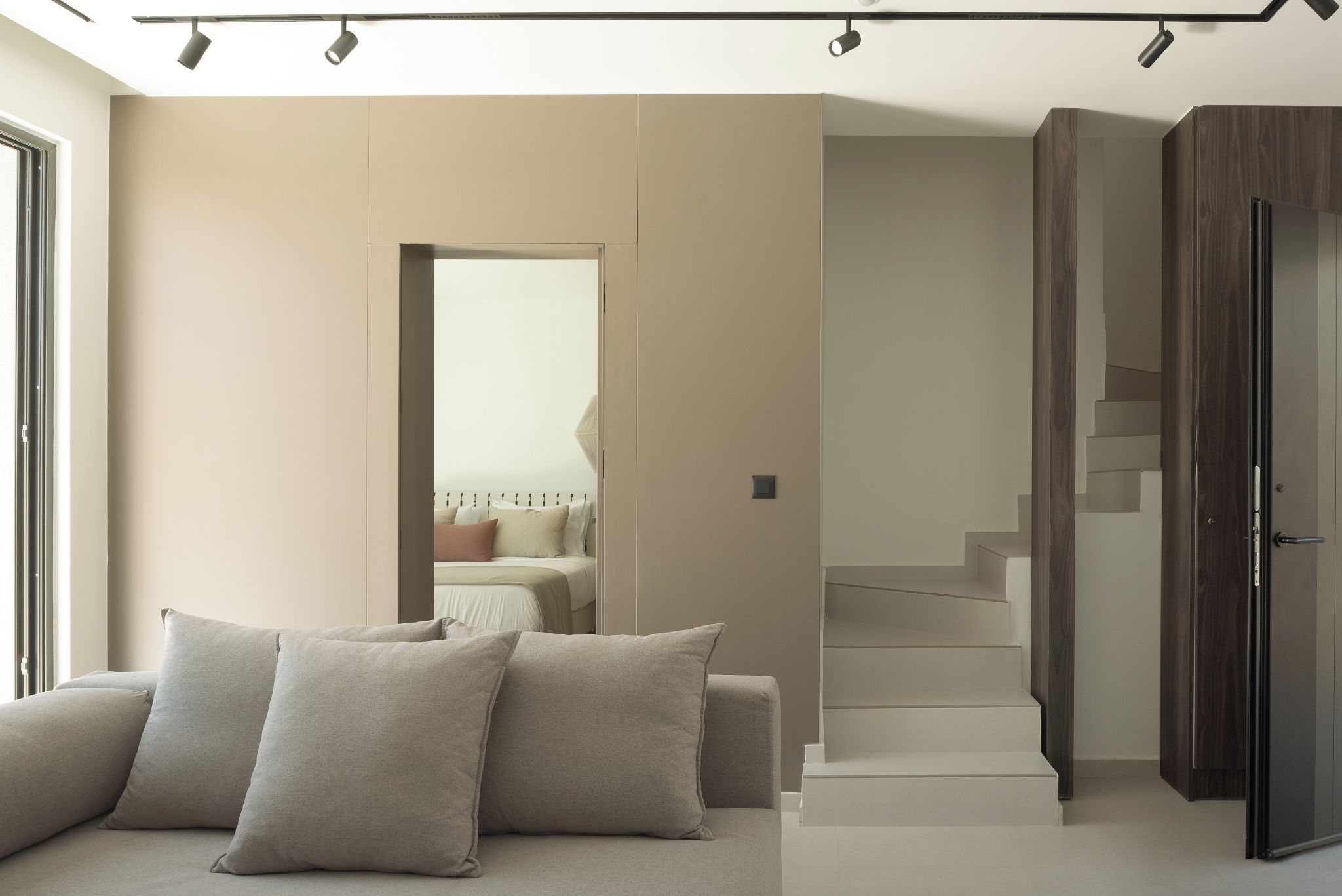 A modern living room with a sofa, a staircase, and a door leading to another room.