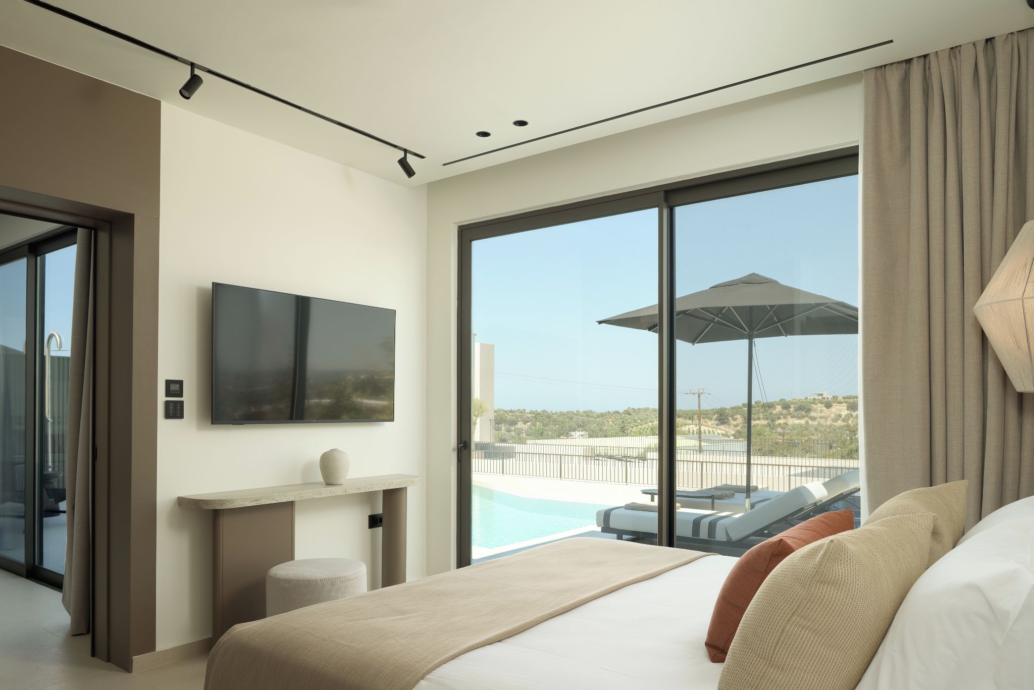 A modern hotel room with a large bed, a television, a view of a pool, and a balcony.