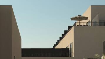A modern building with a staircase leading to a balcony, a large umbrella, and a clear sky.