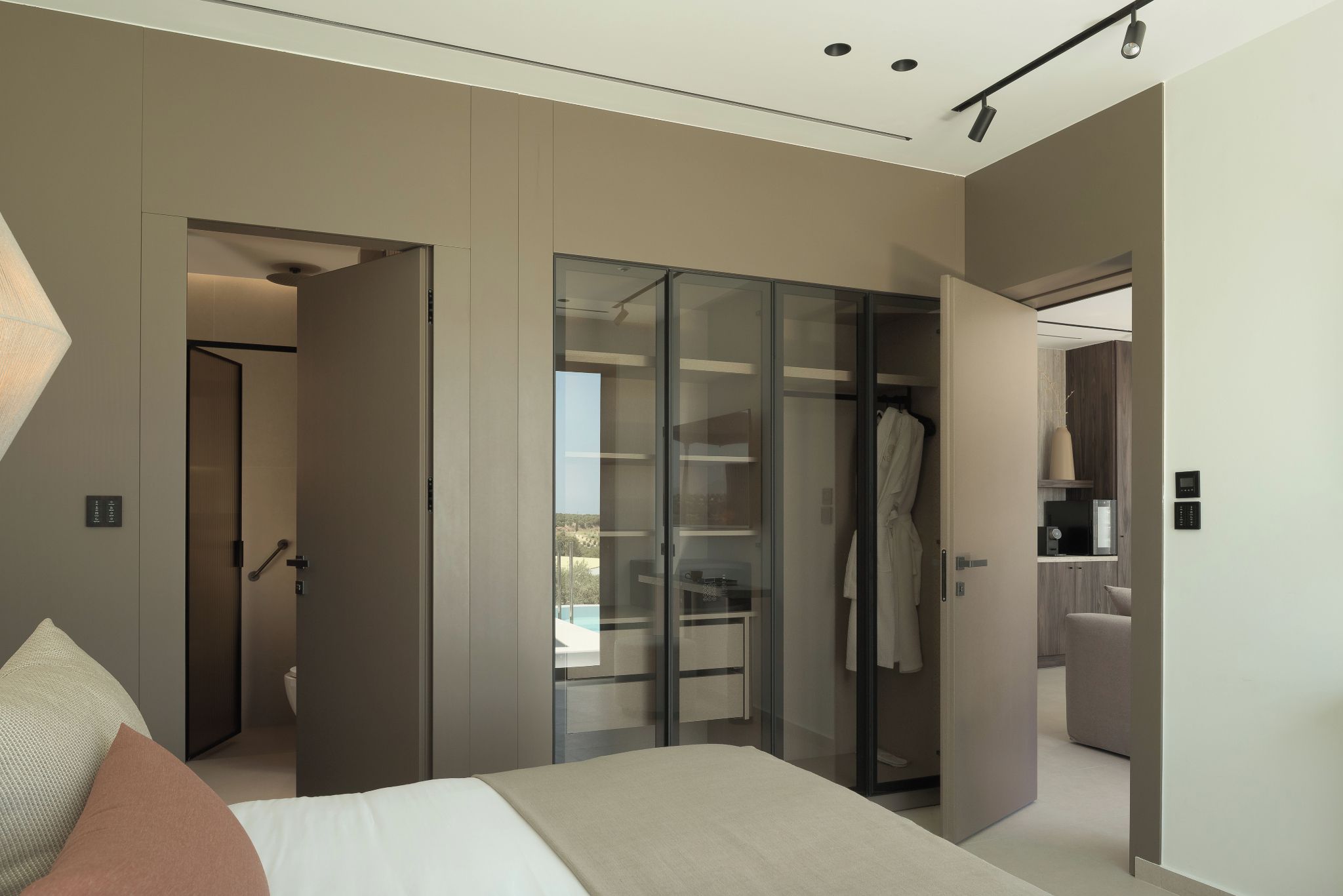 Un dormitorio moderno con cama, vestidor y vistas al exterior.