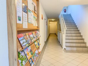A hallway with a corkboard displaying various notices and a bookshelf with magazines. A staircase with a fire extinguisher is visible in the background. - Spacious Alpine holiday apartment on the slopes (Sankt Margarethen im Lungau)